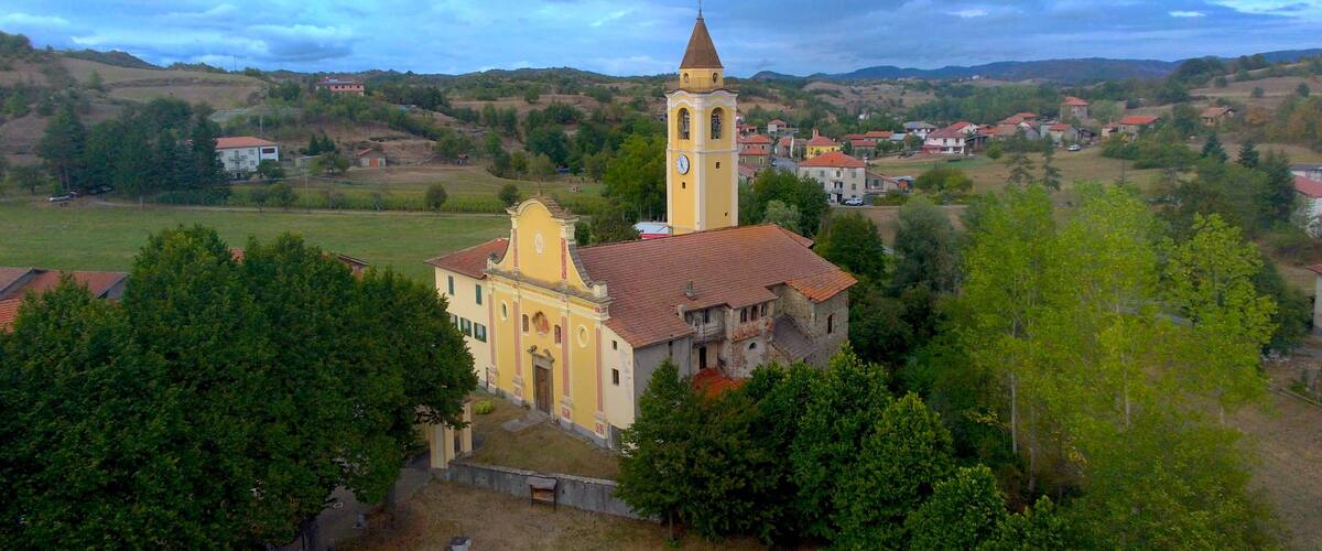 A church with a bell tower surrounded by a rural landscape with houses and trees.