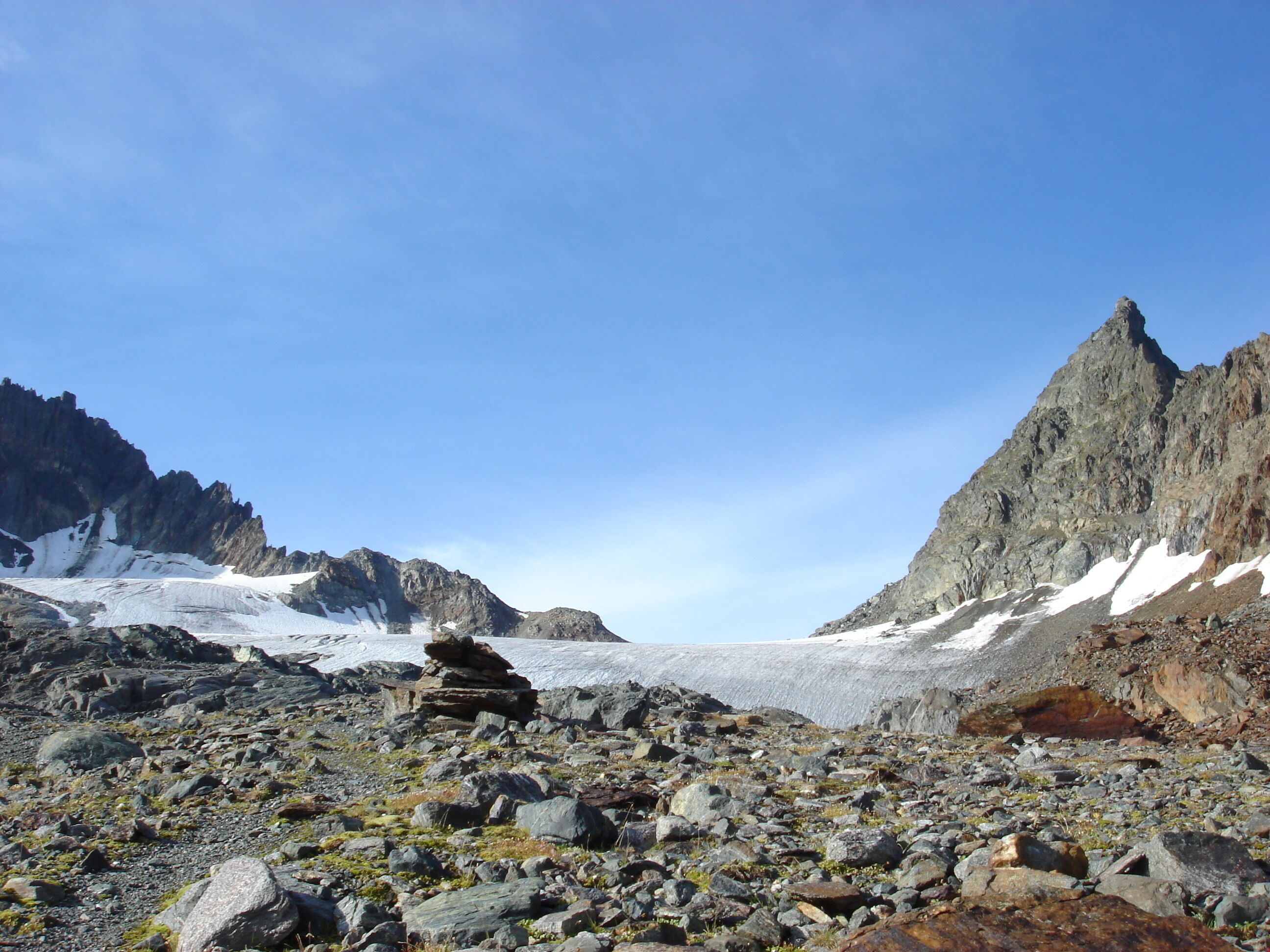 A rocky mountain landscape with a glacier and snow patches.