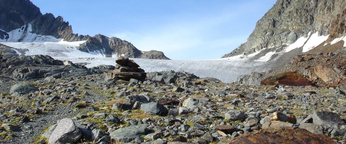 A rocky mountain landscape with a glacier and snow patches.