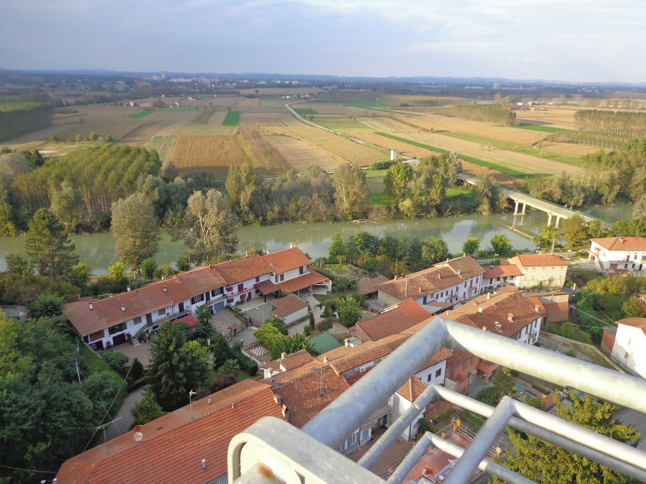 A rural landscape with fields, a river, and traditional buildings with red-tiled roofs.