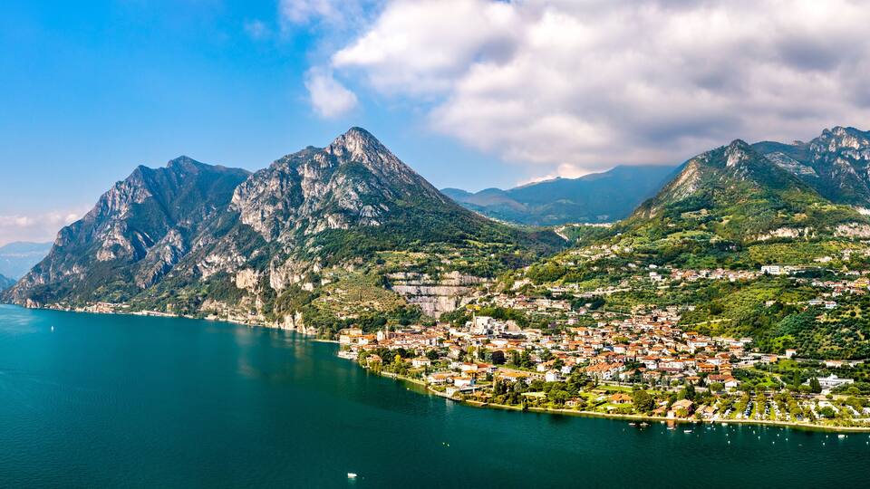 A coastal town nestled between mountains with a clear view of the sea and a prominent peak.