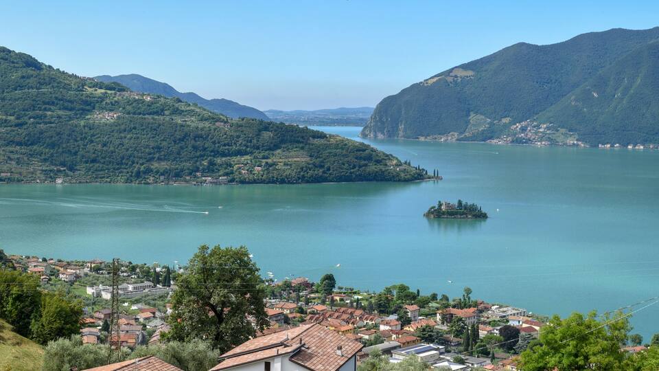 A lake surrounded by mountains, a small island, and a town with red-roofed buildings.