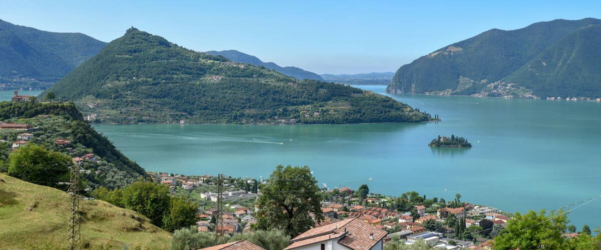 A lake surrounded by mountains, a small island, and a town with red-roofed buildings.