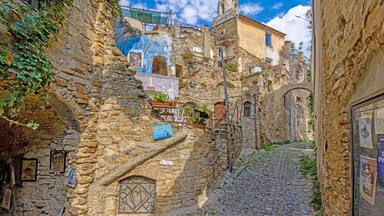 A narrow cobblestone street flanked by stone buildings with signs and posters.