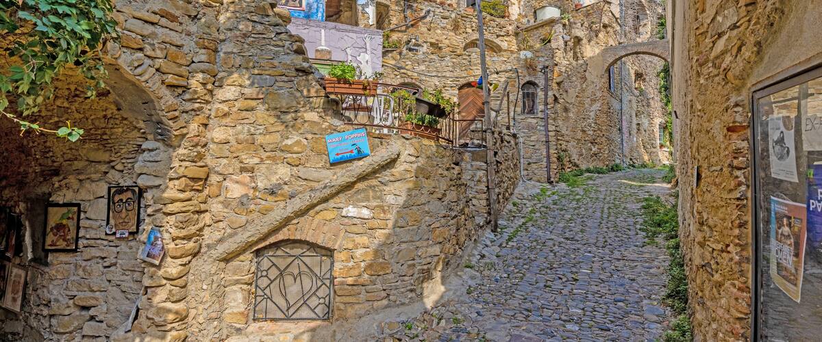 A narrow cobblestone street flanked by stone buildings with signs and posters.