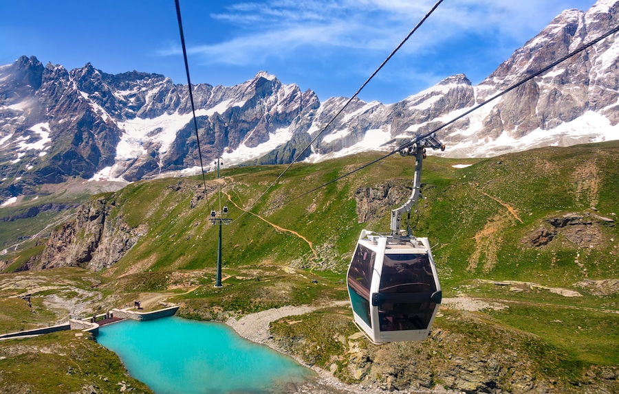 Un teleférico asciende una montaña con un lago turquesa a su base.