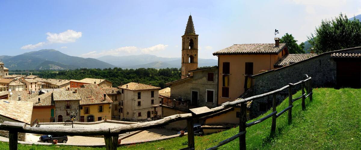 A historic town with stone buildings, a prominent church tower, and mountains in the background.