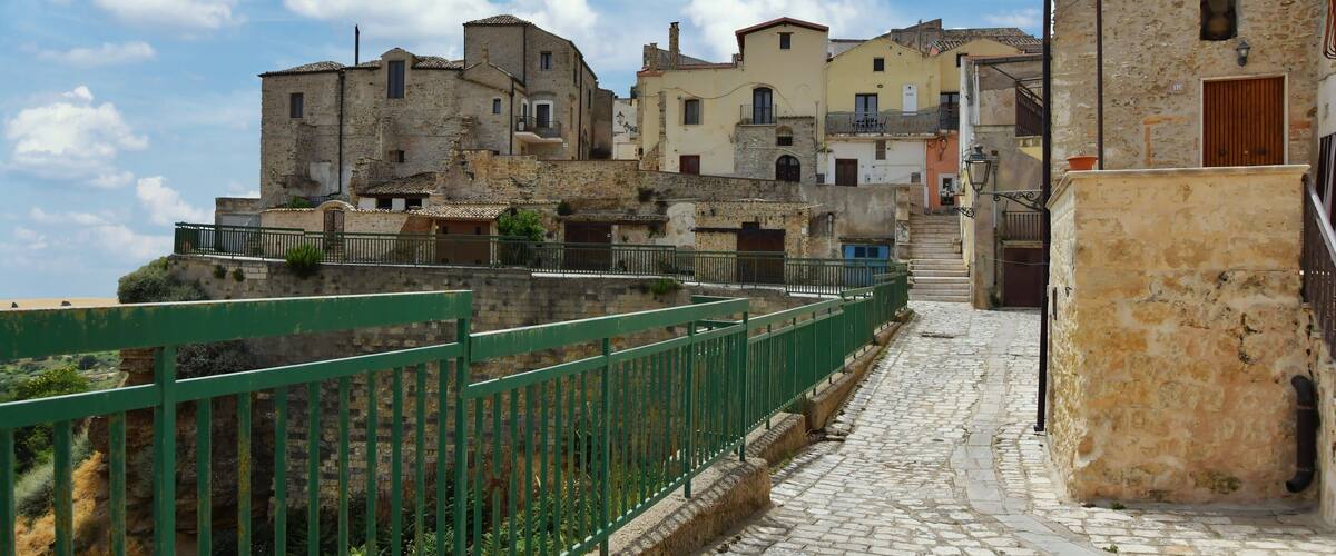 A cobblestone street leading up to a historic town with stone buildings and a green fence.
