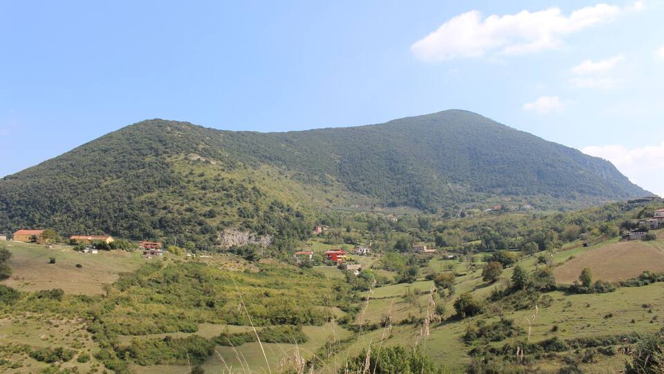 A mountain with a valley, houses, and greenery.