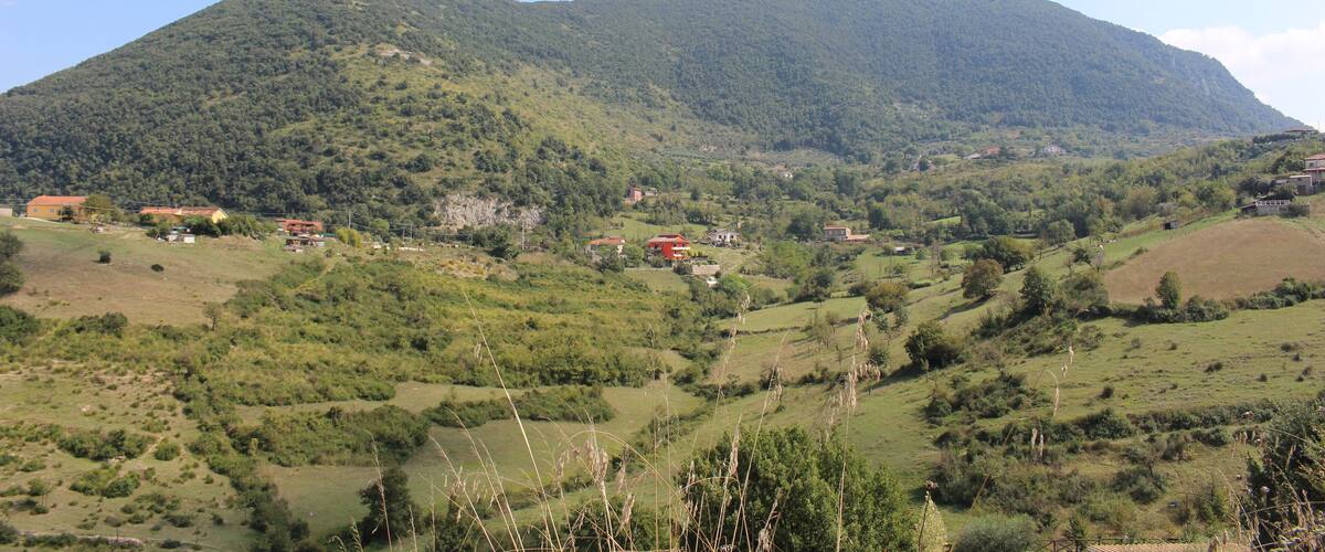 A mountain with a valley, houses, and greenery.