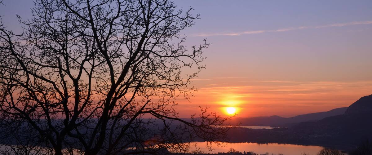 A sunset over a calm lake with silhouetted trees and distant hills.