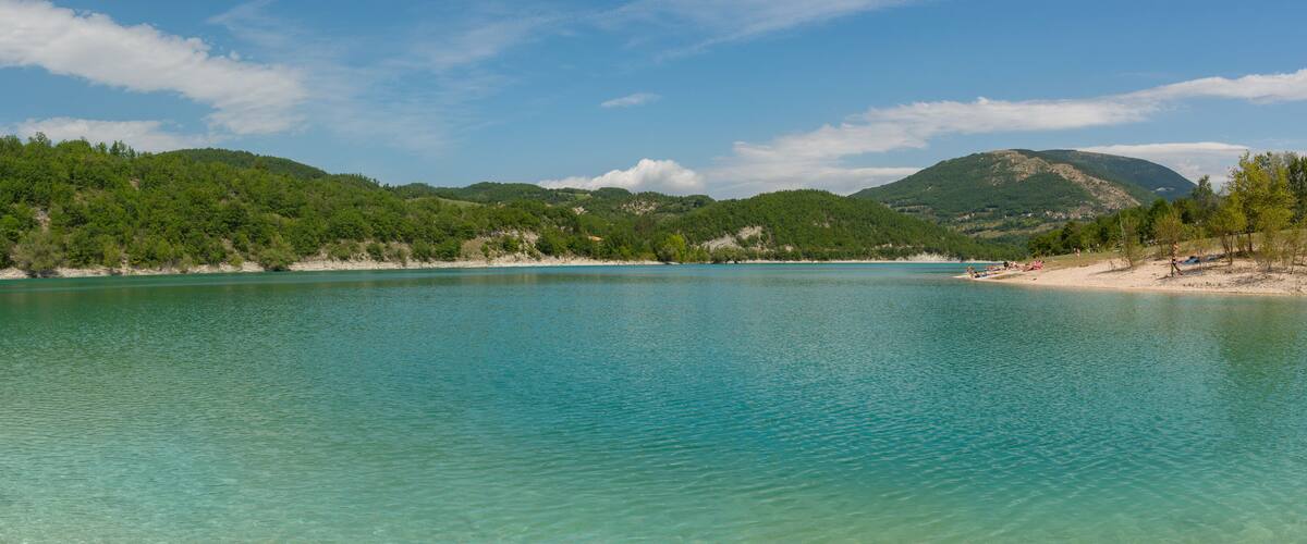 A turquoise lake surrounded by green hills and a clear sky.