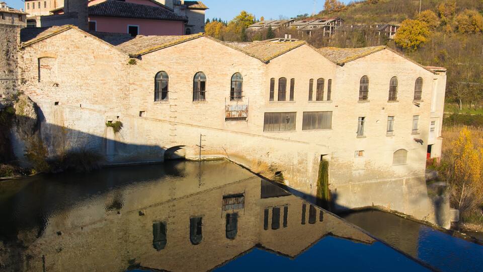 A historic stone building with arched windows and a reflection in the water.