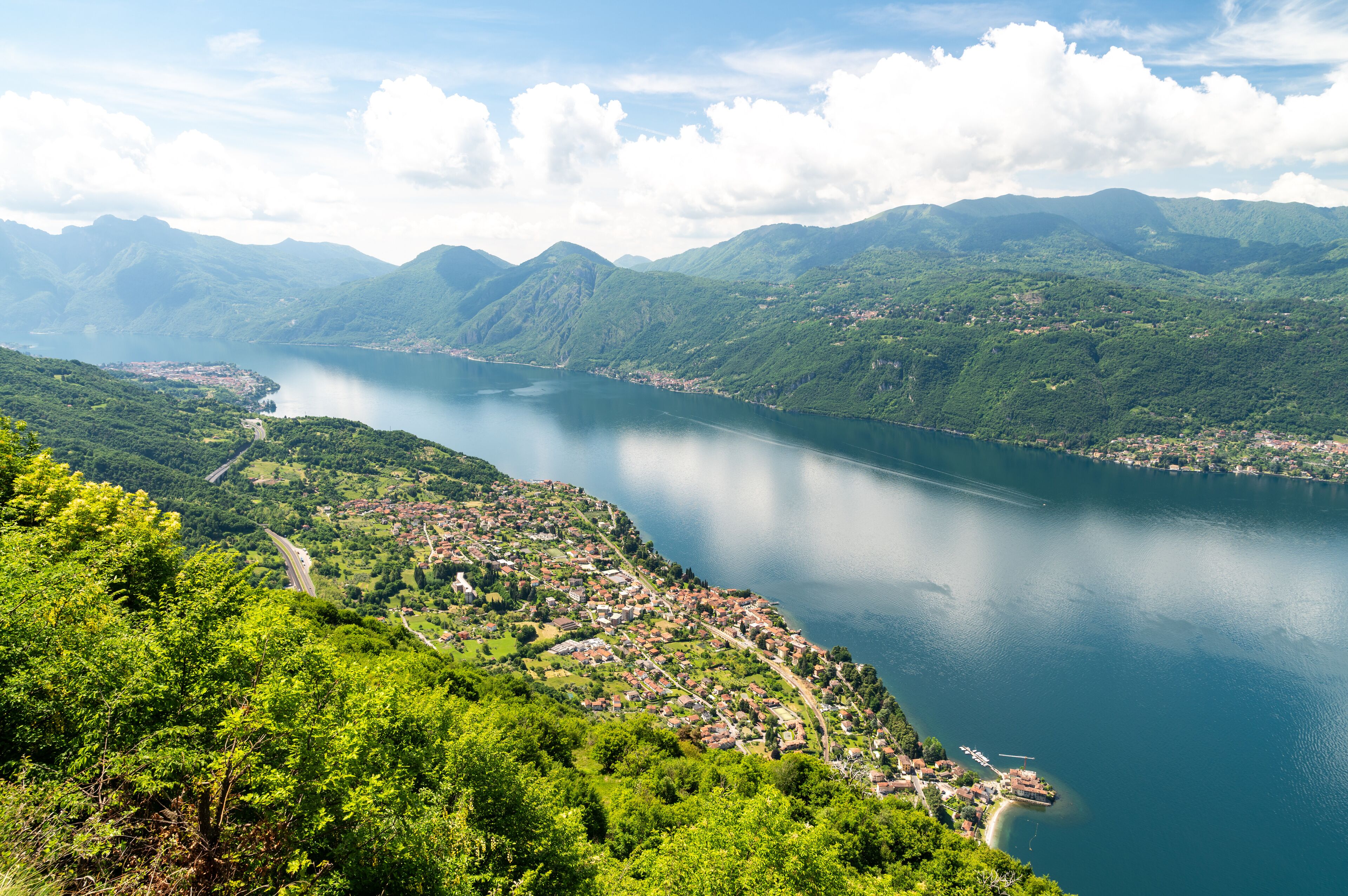 A mountainous landscape with a lake, a winding road, and a small town by the water.