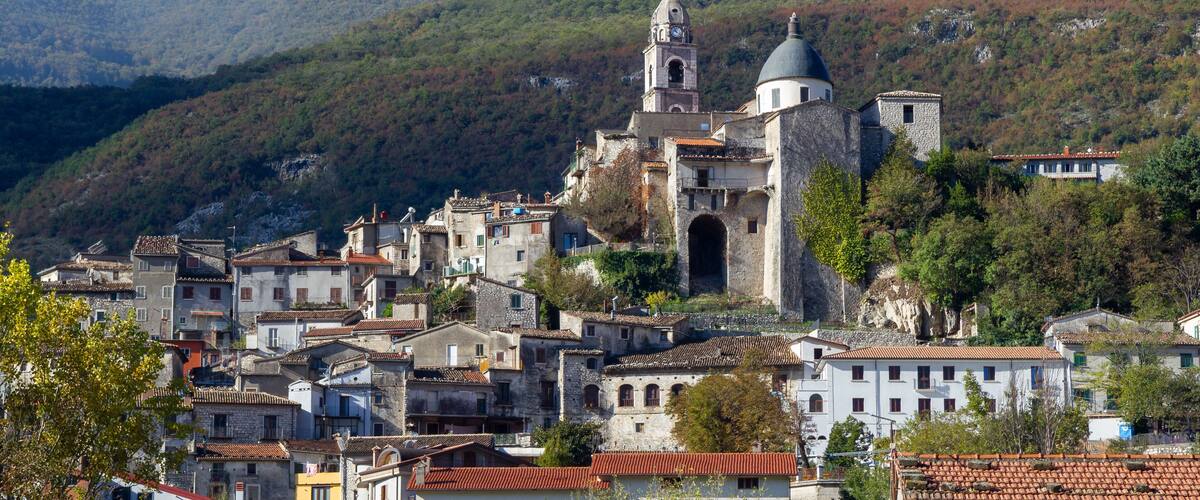 A historic town with a prominent church featuring a bell tower and dome, surrounded by terraced houses and lush green hills.