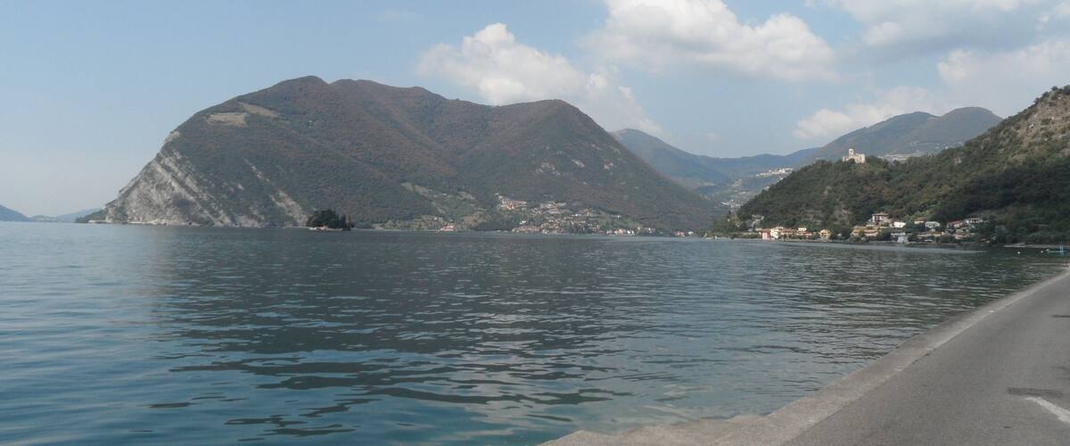 A calm lake with mountains in the background and a road along the shore.