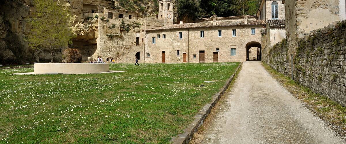 A historic stone building with a tower, a pathway leading to it, and a grassy area with scattered flowers.
