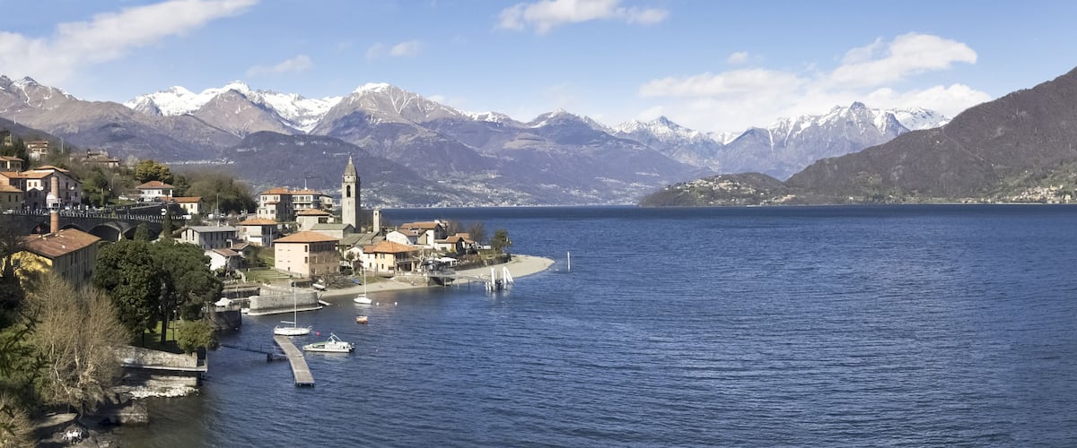 A lakeside town with a prominent church, boats, and snow-capped mountains in the background.