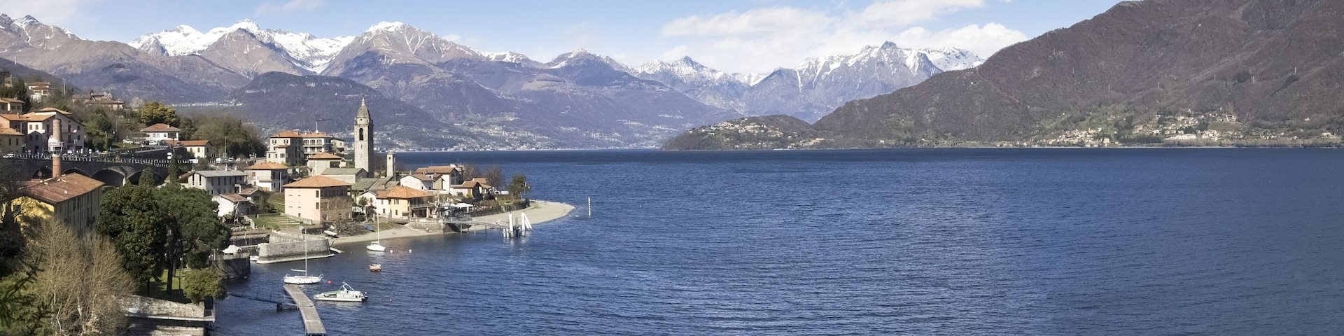 A lakeside town with a prominent church, boats, and snow-capped mountains in the background.