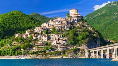 A coastal village with buildings on a hillside, a bridge, and a clear blue sea.
