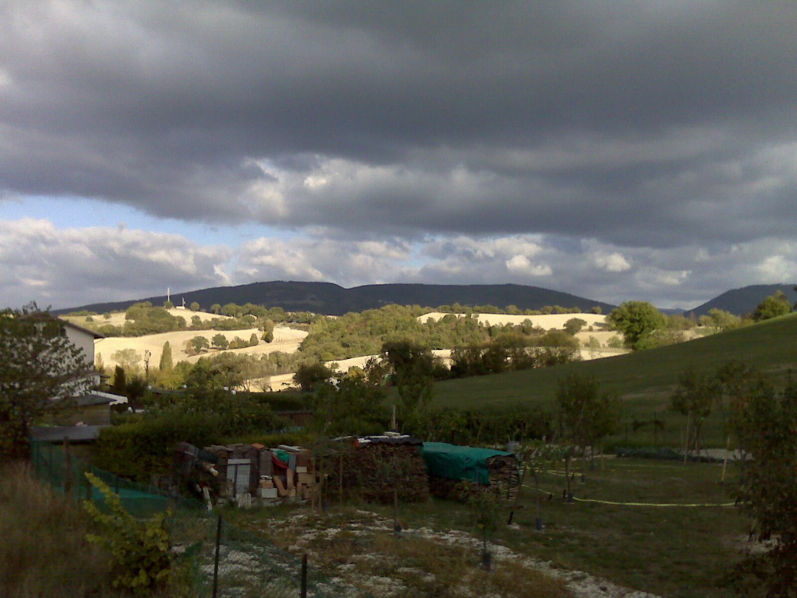 A rural landscape with rolling hills, a farmhouse, and a cloudy sky.