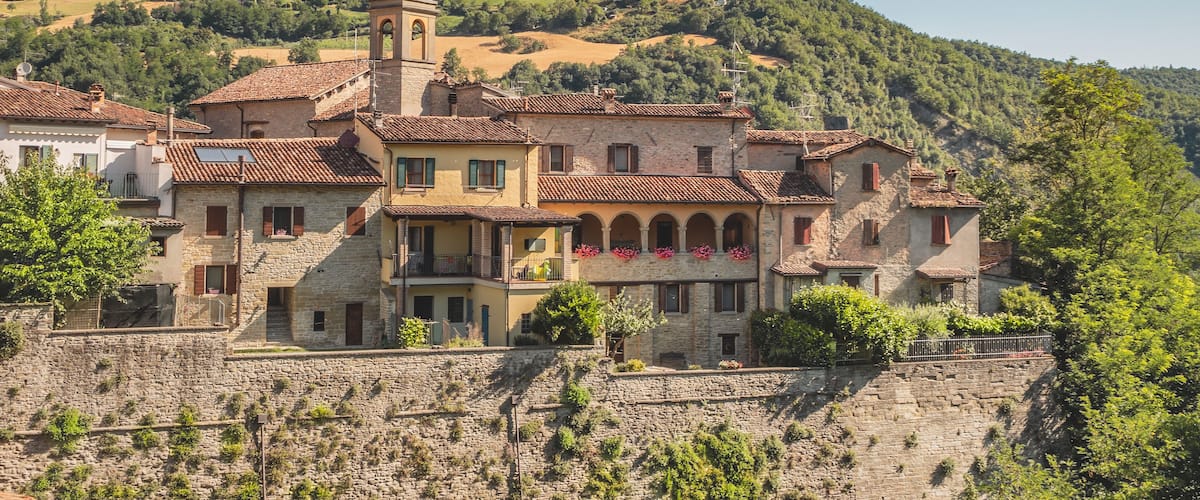 A historic stone building with a bell tower, surrounded by lush green hills and terraced vineyards.