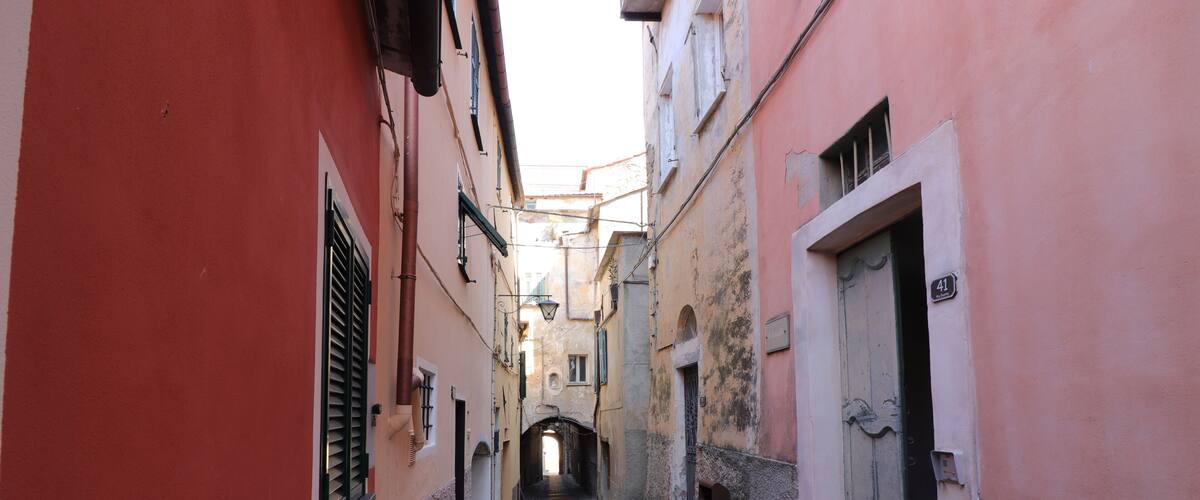 A narrow cobblestone alley flanked by buildings with pink and white facades, a visible door with the number 41, and a small archway at the end.