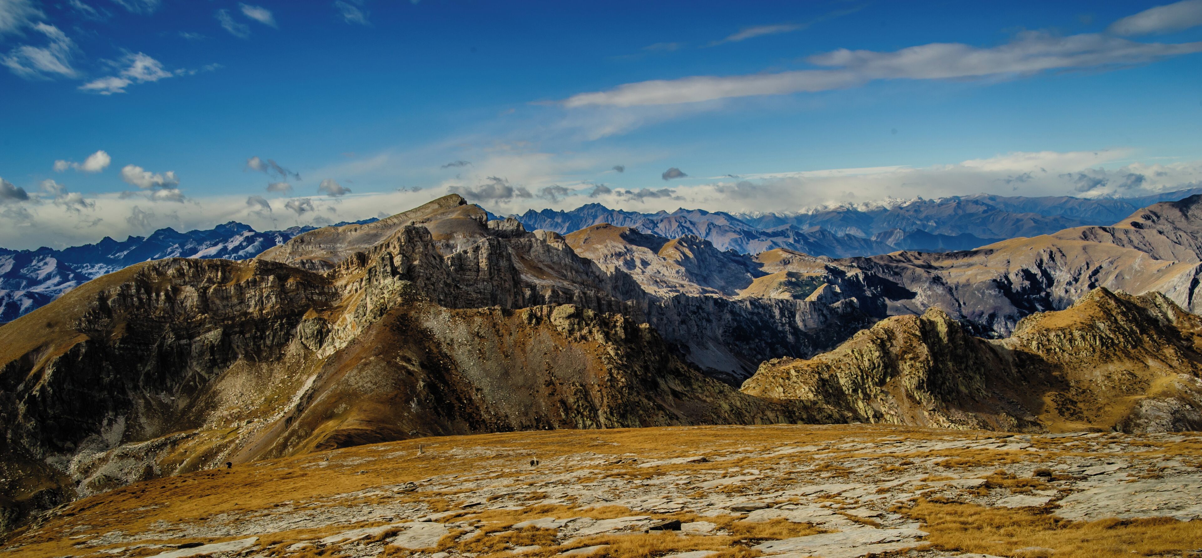A mountainous landscape with rocky terrain and distant snow-capped peaks under a clear blue sky.
