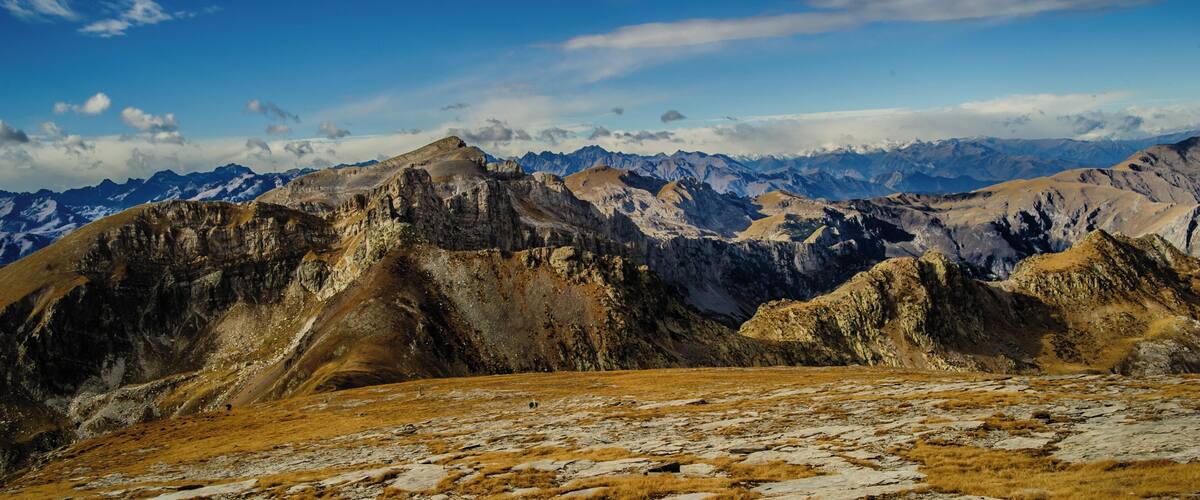 A mountainous landscape with rocky terrain and distant snow-capped peaks under a clear blue sky.