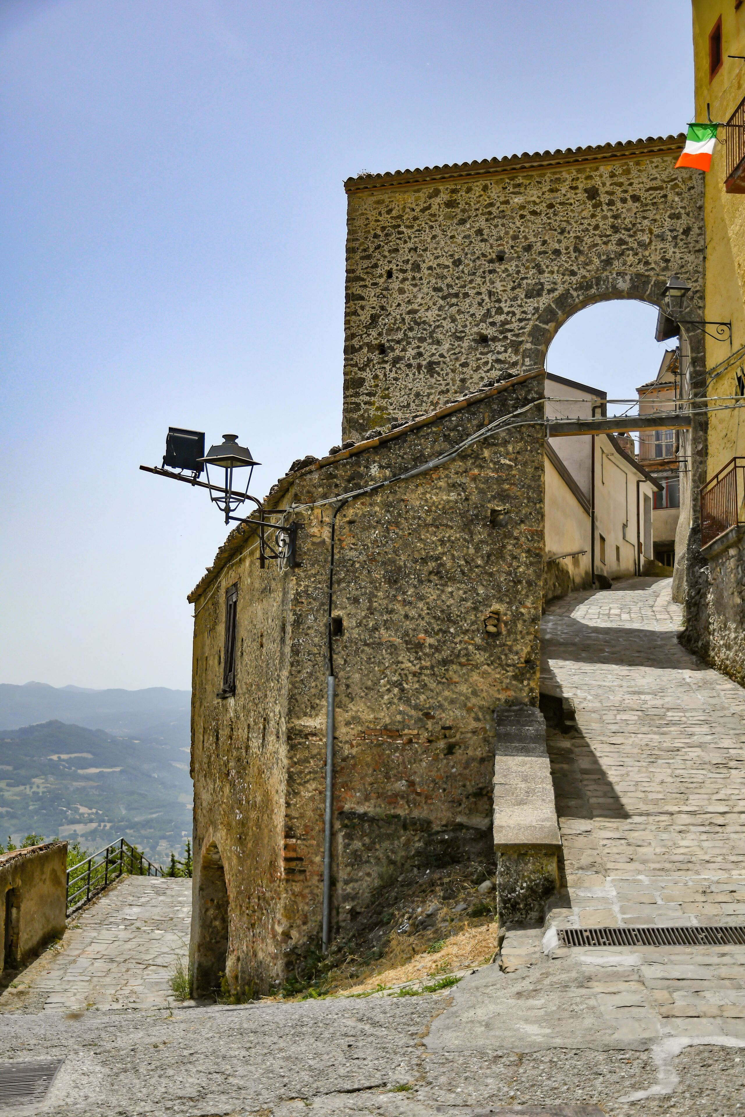 A stone staircase leading up to a stone archway, with a flag on the right and a street lamp on the left.