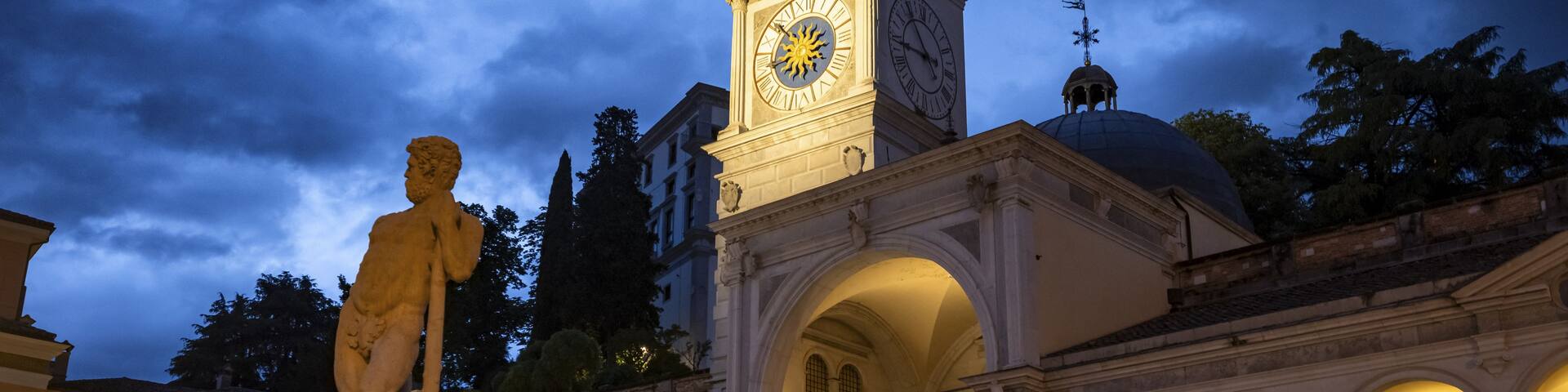 A historic square with a statue, a clock tower, and classical architecture.