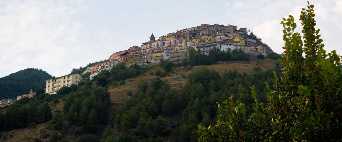A hillside town with colorful buildings, dense greenery, and a clear sky.