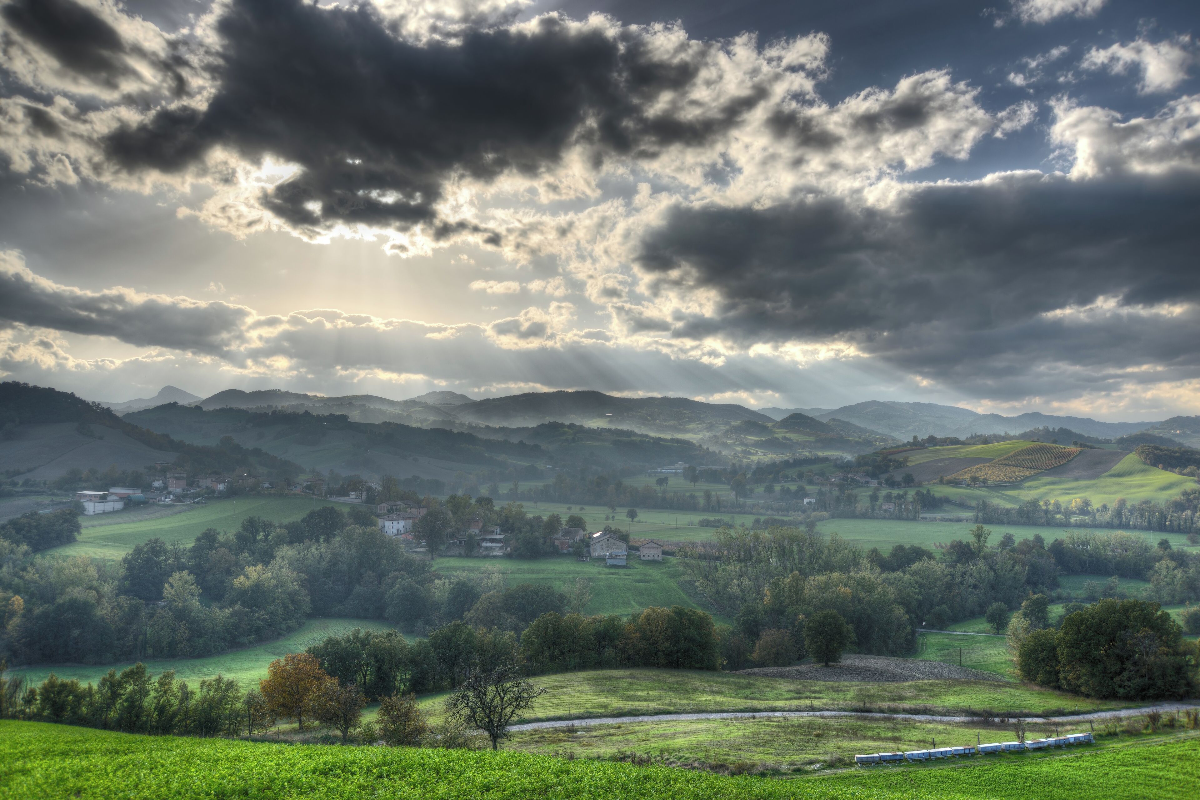 Ländliche Landschaft mit sanften Hügeln, verstreuten Häusern und einer Bahnstrecke.