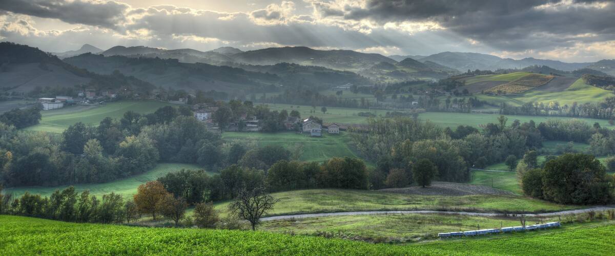 Ländliche Landschaft mit sanften Hügeln, verstreuten Häusern und einer Bahnstrecke.