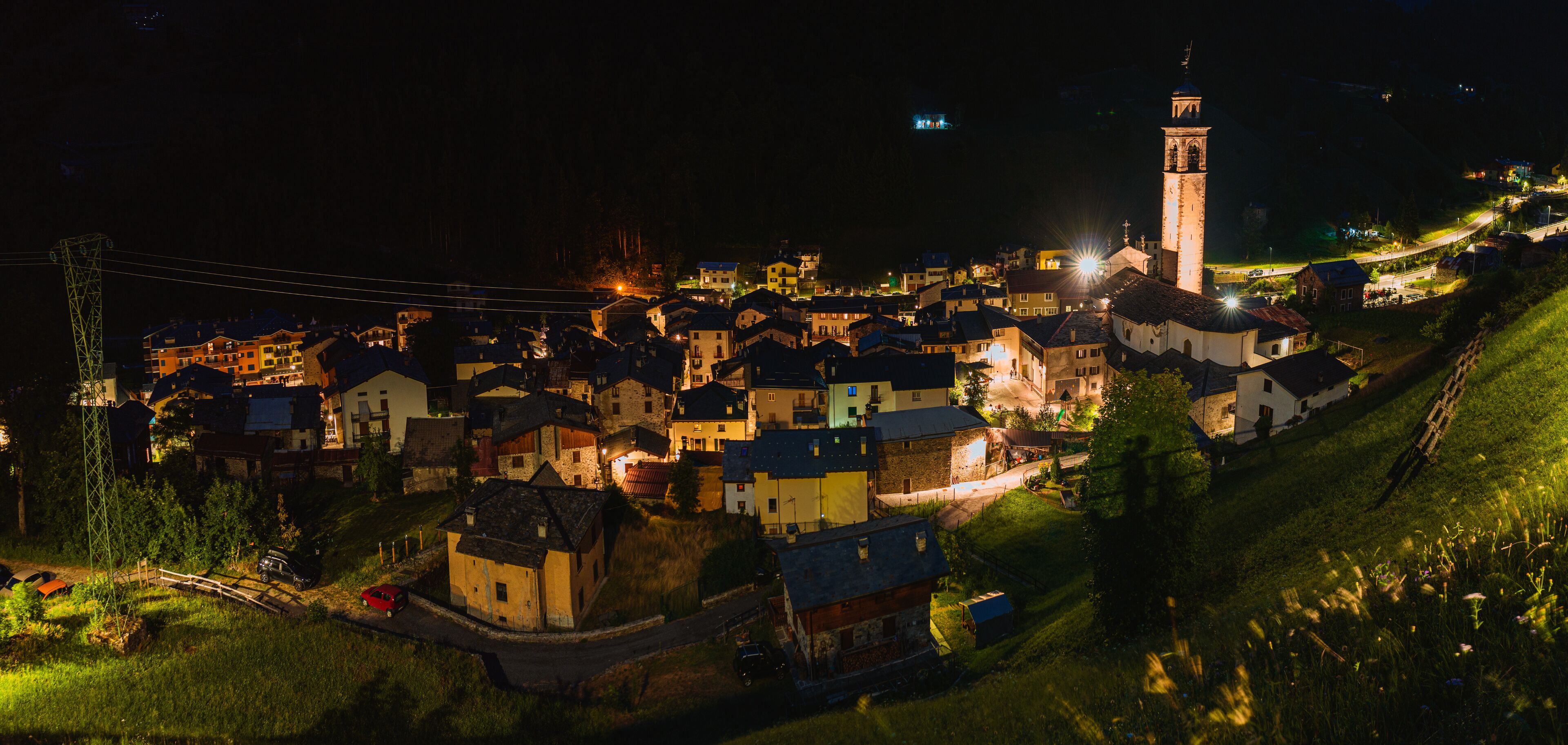 A village at night with illuminated buildings, a prominent tower, and a winding road.
