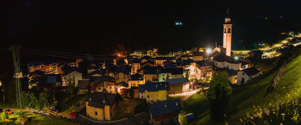 A village at night with illuminated buildings, a prominent tower, and a winding road.