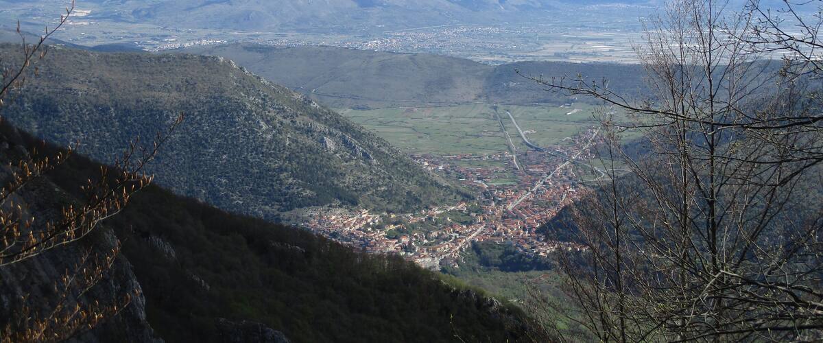 A mountainous landscape with a valley, a town, and distant snow-capped mountains.