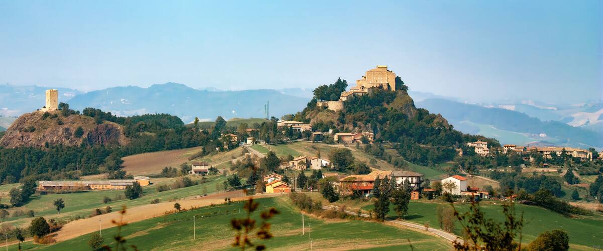A historic town with a prominent castle on a hill, surrounded by lush green fields and rolling hills.