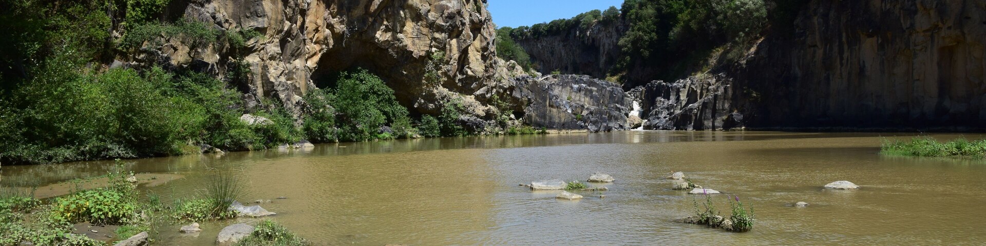 A river with rocky banks and a forested cliff.