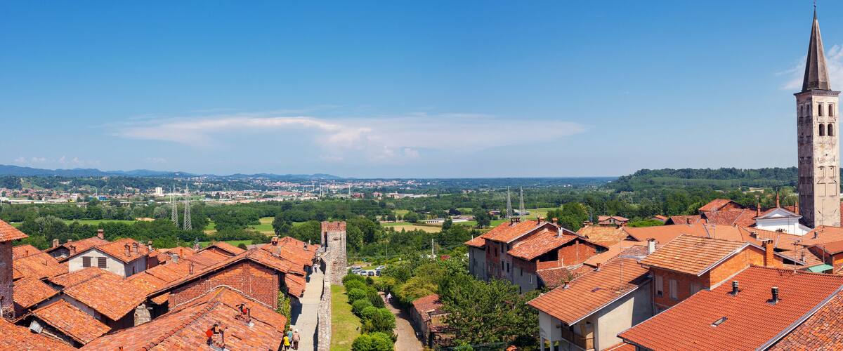 A town with red-tiled rooftops, a prominent church tower, and a view of distant mountains and fields.