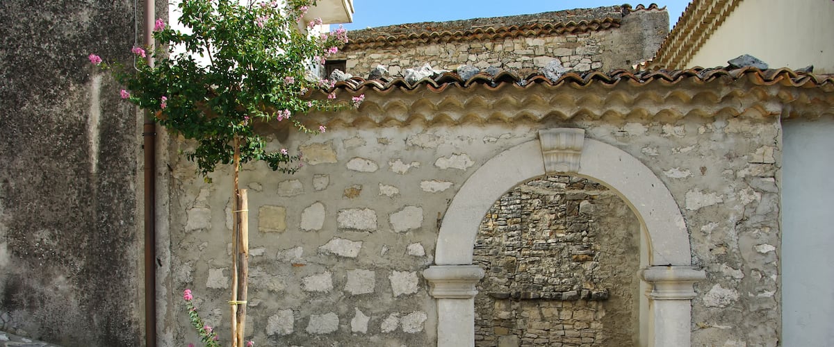 A stone archway with a tiled roof, steps leading up to it, and a small tree with pink flowers.