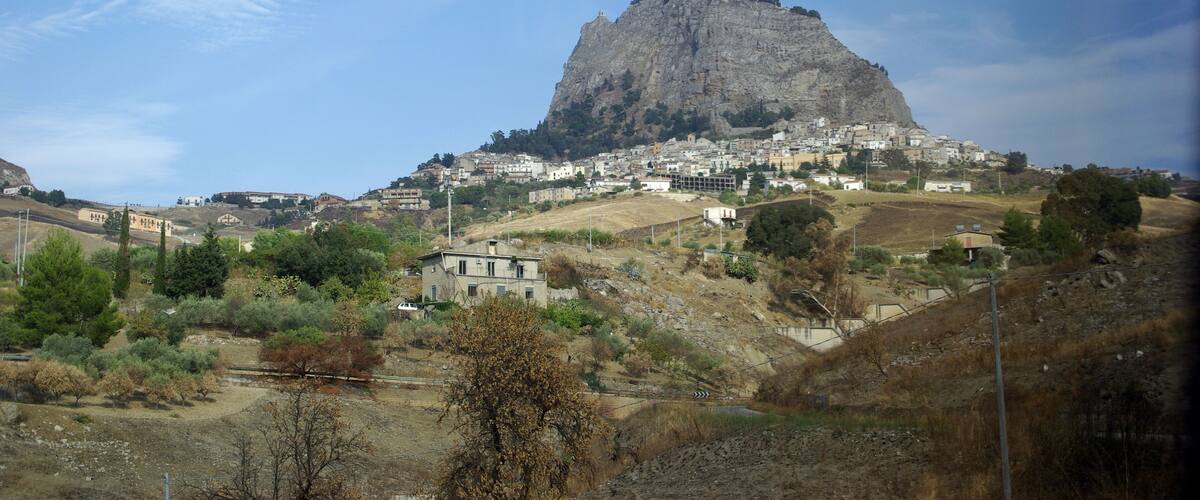 A town nestled on a hillside with a prominent rocky hill in the background.