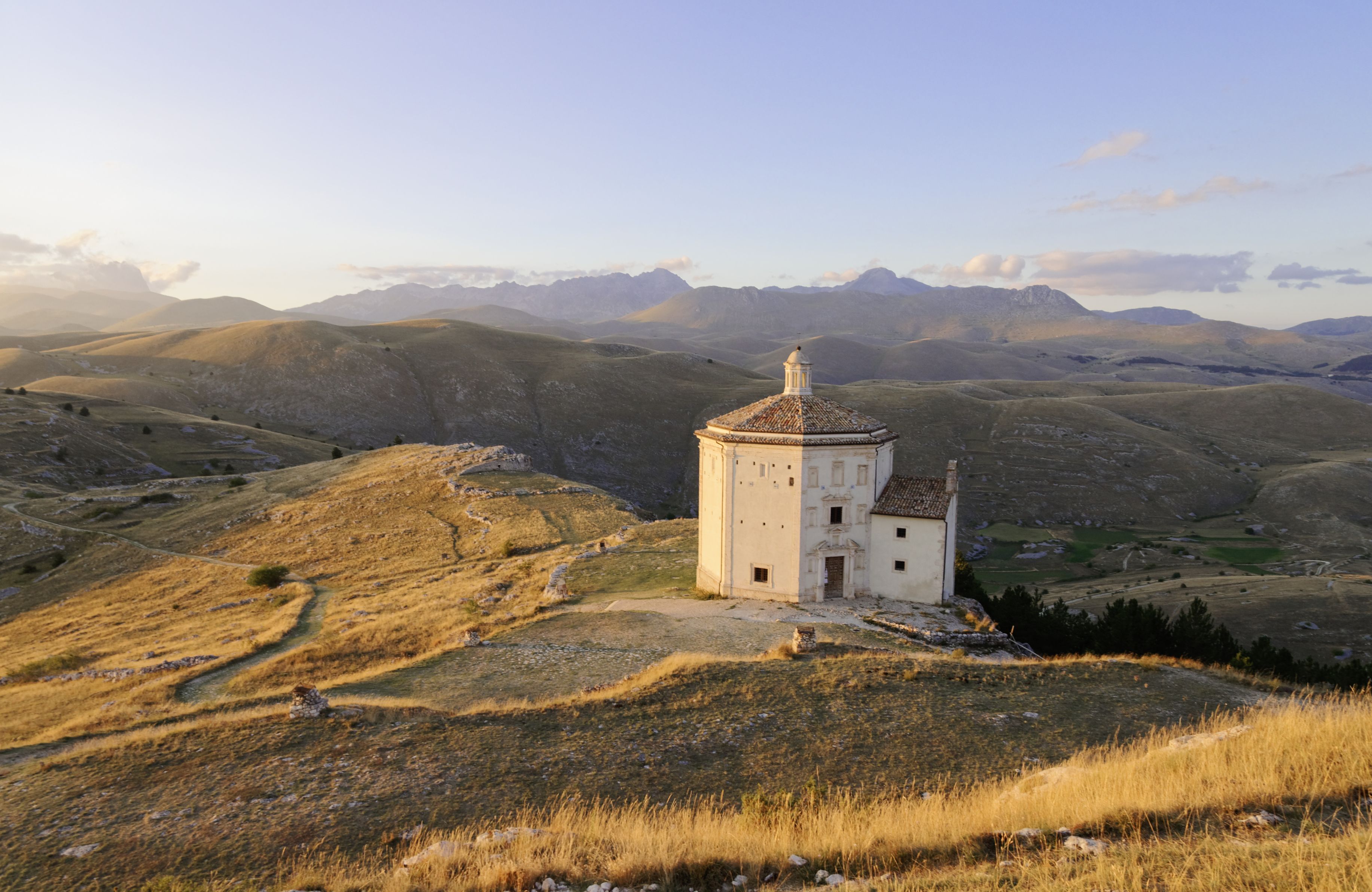 A white church with a dome, surrounded by rolling hills and mountains in the background.