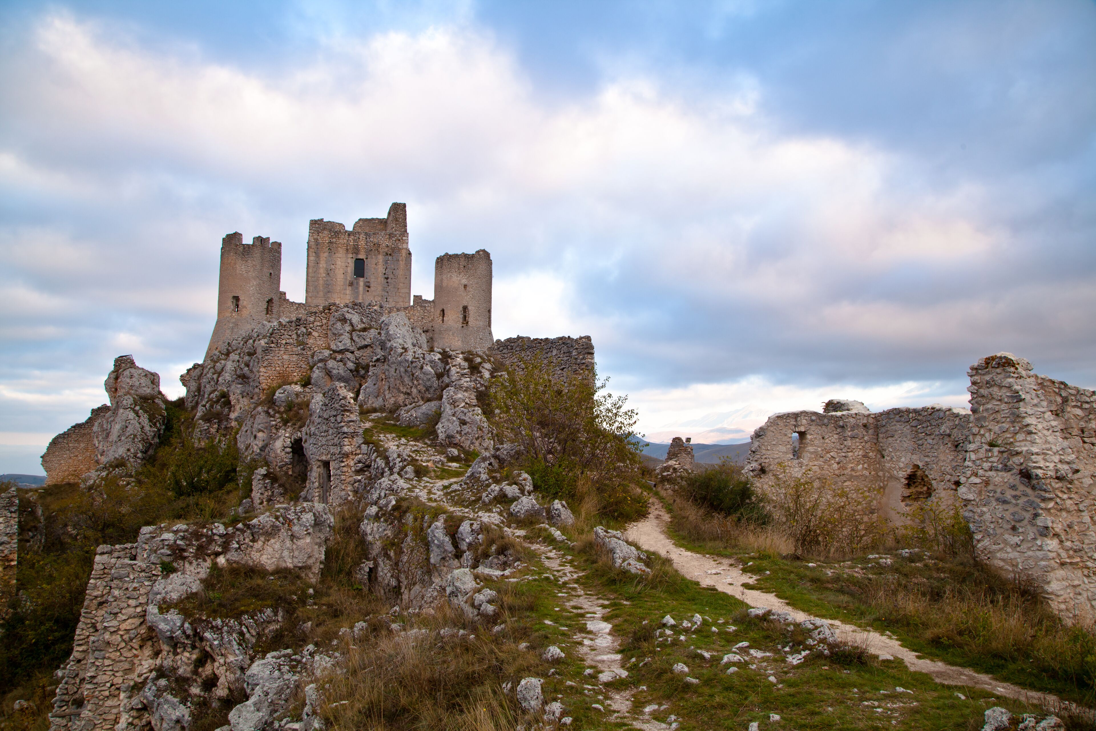 A medieval castle ruins on a hill with a path leading to it.