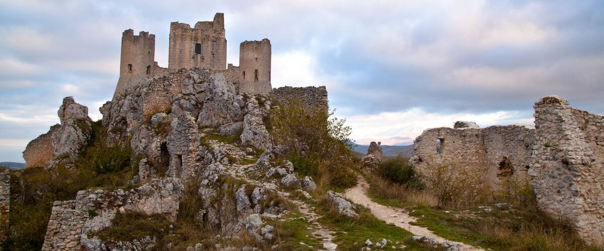 A medieval castle ruins on a hill with a path leading to it.