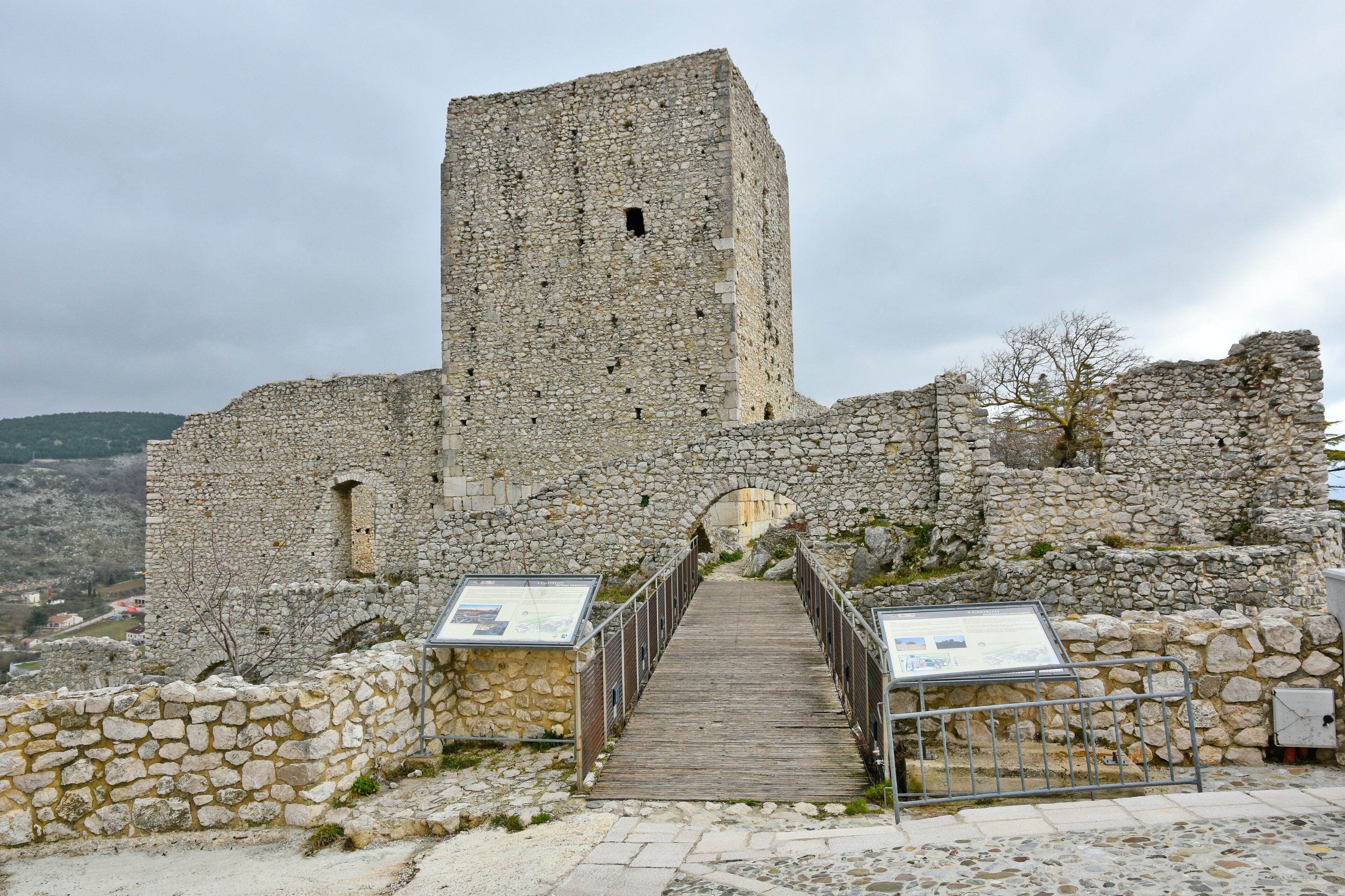 A stone castle with a tall tower and a wooden pathway leading to an arched entrance.