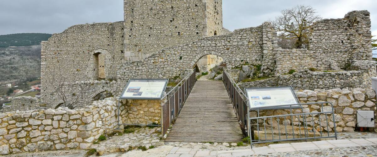 A stone castle with a tall tower and a wooden pathway leading to an arched entrance.