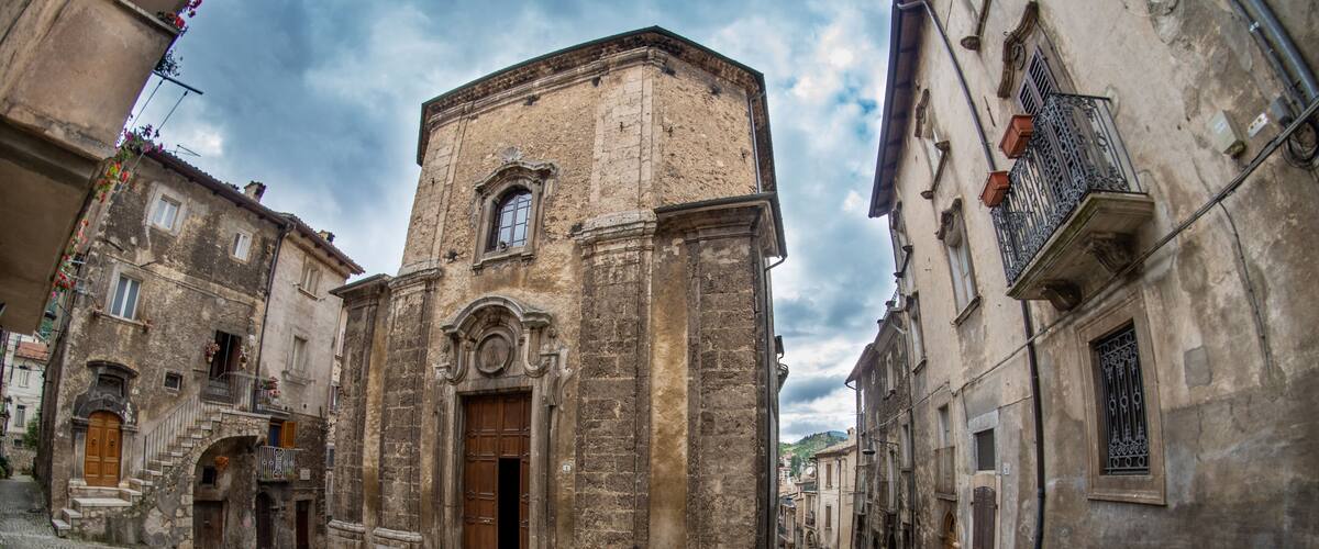 A cobblestone street flanked by historic buildings with a prominent church featuring a wooden door and a bell tower.