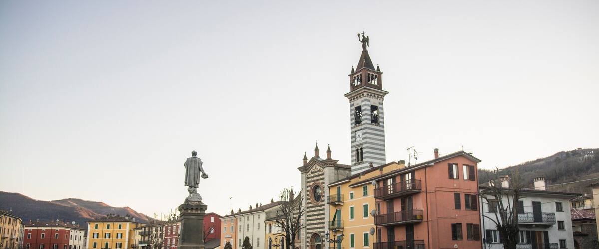 A square with a statue, a clock tower, and colorful buildings.