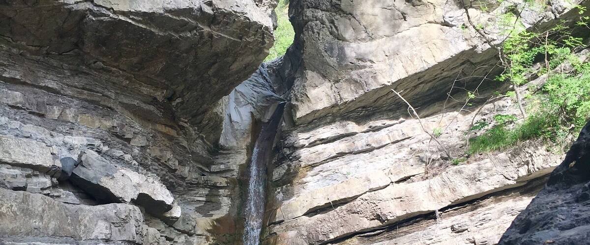 A waterfall cascading down a rocky cliff into a pool surrounded by large boulders and greenery.